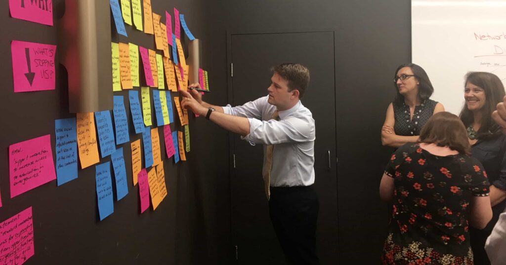 A participant adds sticky notes to the wall to contribute to the exercise known as challenge mapping